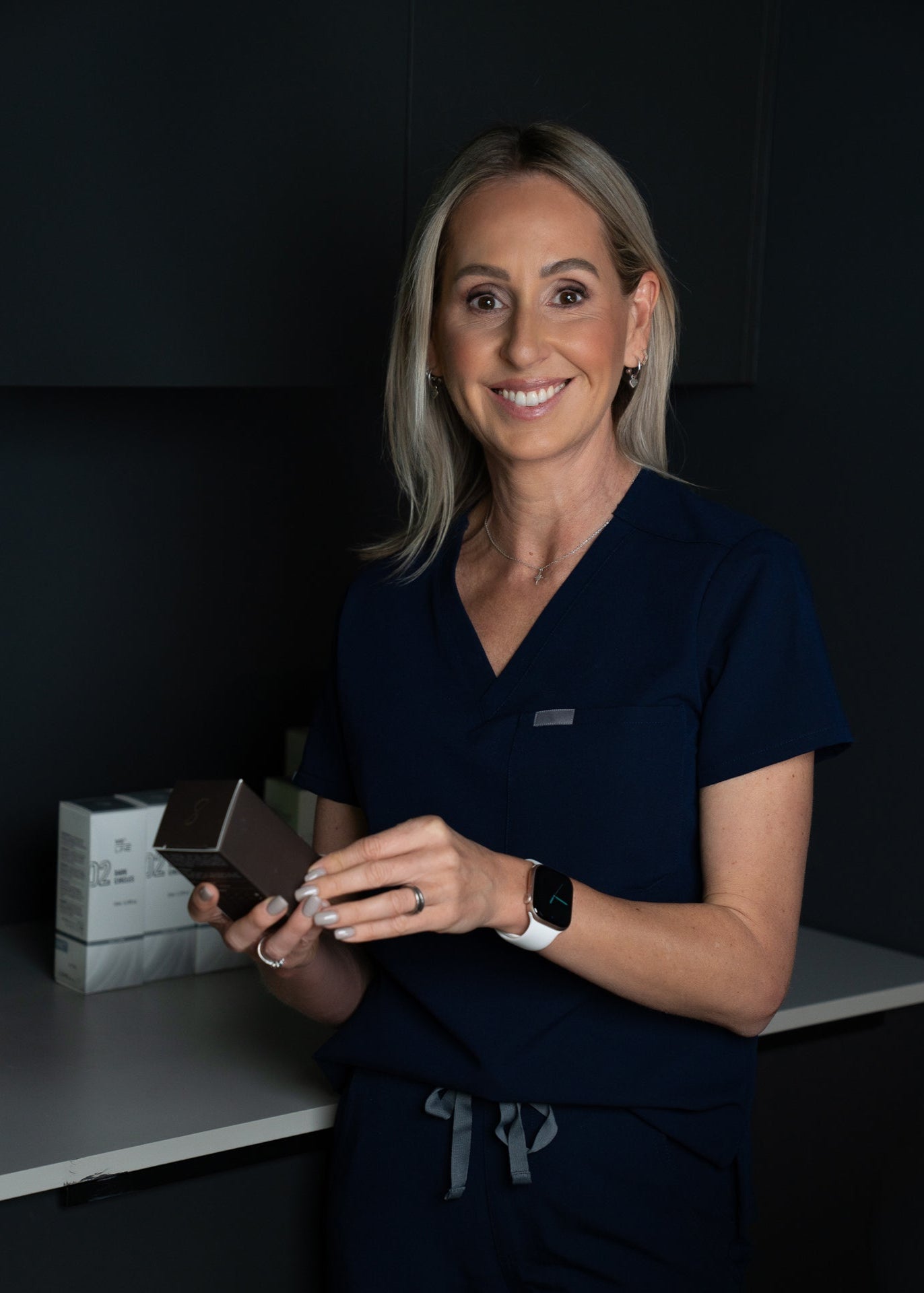 Kath Candy in dark scrubs holding a smartphone in a medical setting